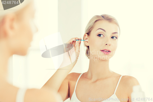 Image of woman cleaning ear with cotton swab at bathroom