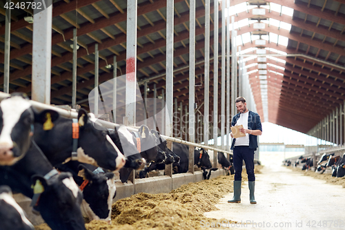 Image of farmer with clipboard and cows in cowshed on farm