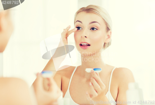 Image of young woman putting on contact lenses at bathroom