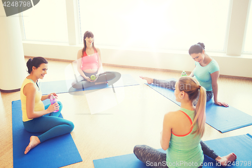 Image of happy pregnant women sitting on mats in gym