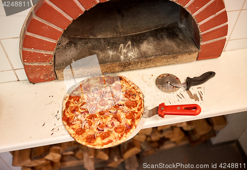 Image of baked pizza on peel and cutter at pizzeria oven 