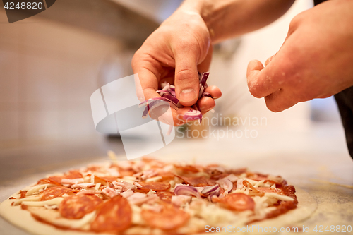 Image of cook adding onion to salami pizza at pizzeria