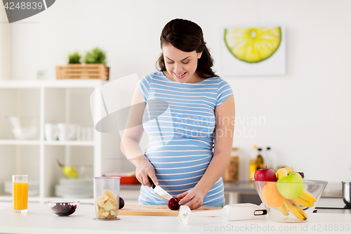 Image of pregnant woman chopping fruits at home kitchen