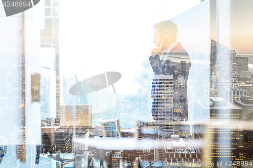 Image of Businessman talking on a mobile phone while looking through window in NY