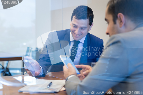 Image of Two businessmen using smart phones and touchpad at meeting.