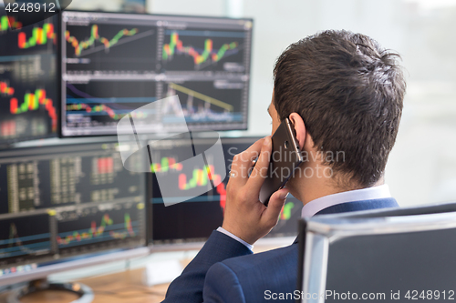 Image of Over the shoulder view of stock broker trading online, talking on mobile phone.