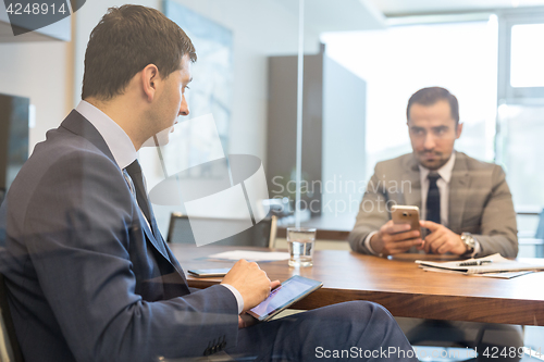 Image of Two businessmen using smart phones and touchpad at meeting.