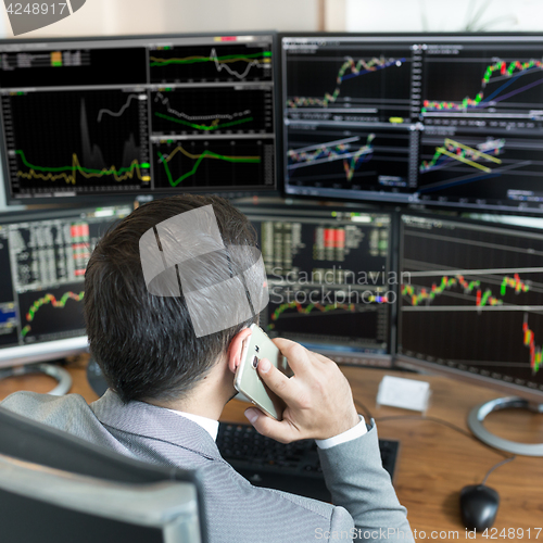 Image of Over the shoulder view of stock broker trading online, talking on mobile phone.