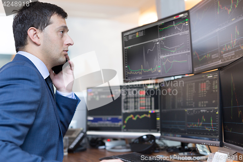 Image of Stock broker trading online, talking on mobile phone.