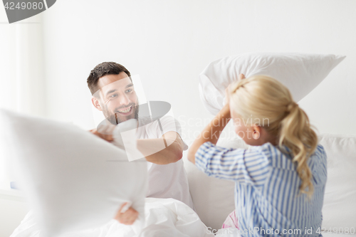Image of happy couple having pillow fight in bed at home