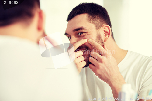 Image of smiling man squeezing pimple at bathroom mirror