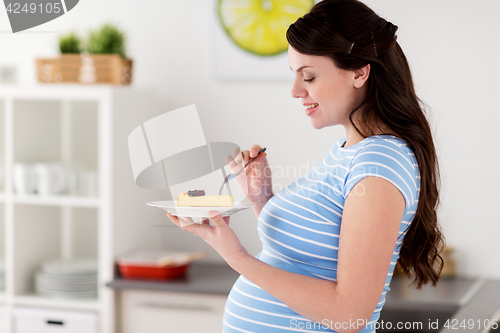 Image of happy pregnant woman eating cake at home kitchen