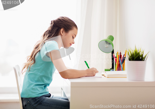 Image of happy girl with book writing to notebook at home