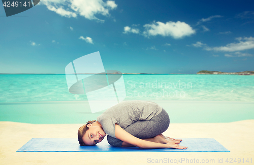 Image of happy woman making yoga in child pose on beach 
