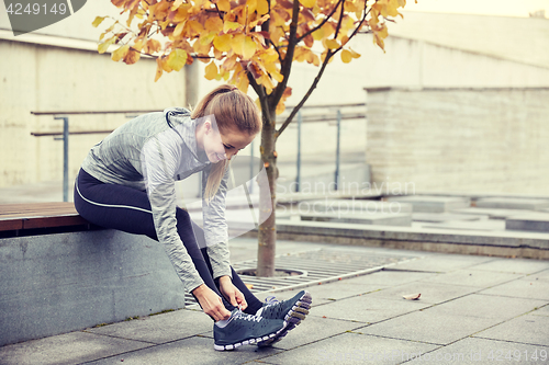 Image of happy young sporty woman tying shoelaces outdoors