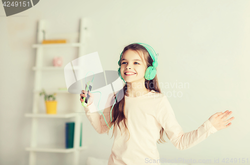 Image of girl jumping on bed with smartphone and headphones