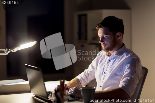 Image of man with laptop and coffee working at night office