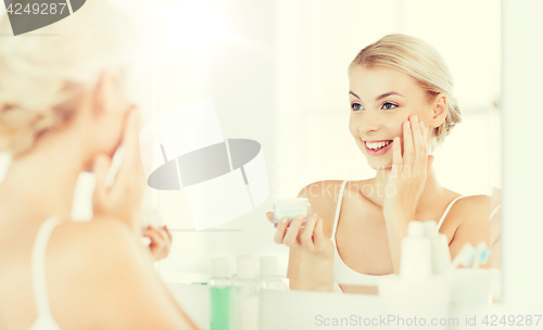 Image of happy woman applying cream to face at bathroom