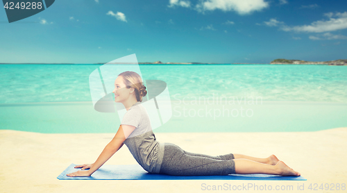 Image of woman making yoga in dog pose on beach 