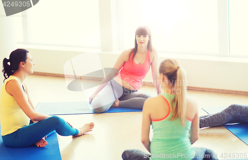 Image of happy pregnant women sitting on mats in gym