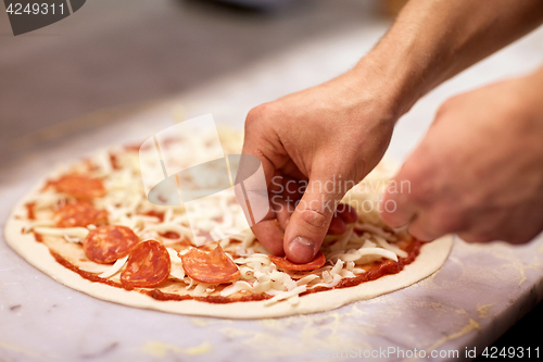 Image of cook hands adding salami to pizza at pizzeria