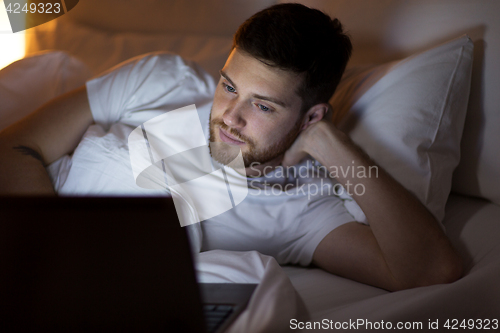 Image of young man with laptop in bed at home bedroom