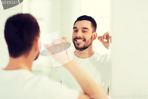 Image of man cleaning ear with cotton swab at bathroom