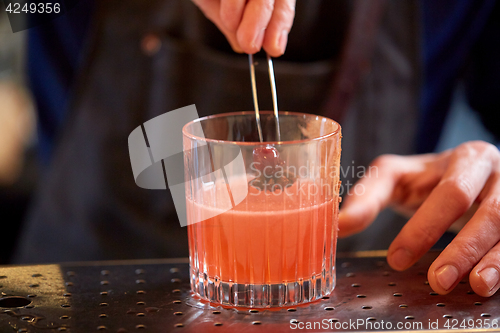 Image of bartender with glass of cocktail and cherry at bar