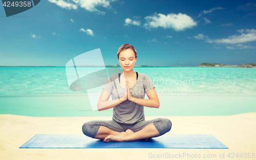 Image of woman meditating in lotus yoga pose on beach 