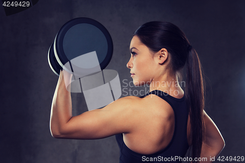 Image of young woman flexing muscles with dumbbells in gym