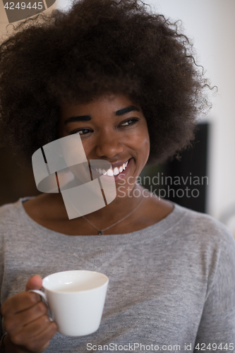 Image of black woman drinking coffee in front of fireplace