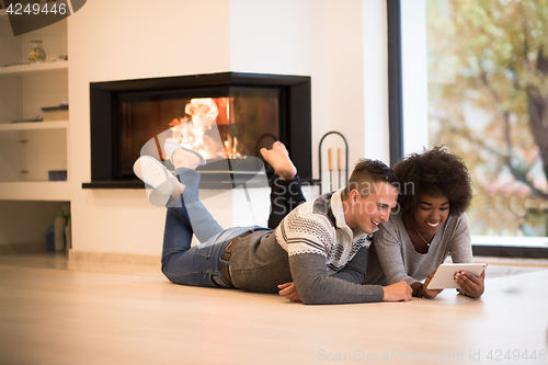 Image of multiethnic couple using tablet computer on the floor
