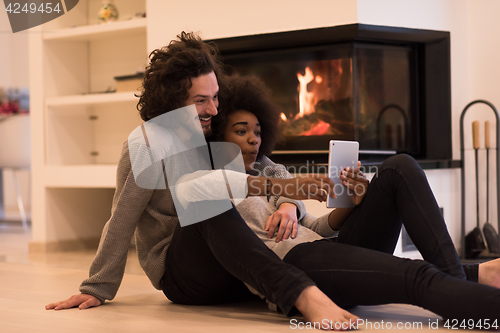 Image of multiethnic couple using tablet computer on the floor