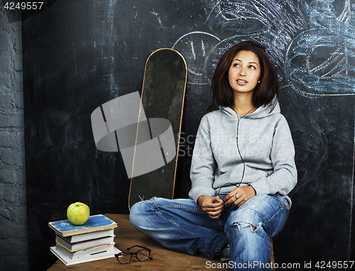 Image of young cute teenage girl in classroom at blackboard seating on ta