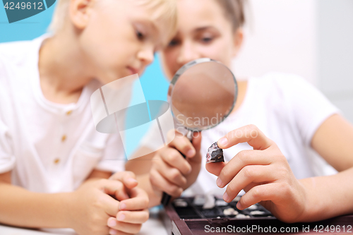 Image of Casket minerals, a collection of stones. Siblings watching stones under a magnifying glass. Malachite, a child watching a collection of rocks and minerals