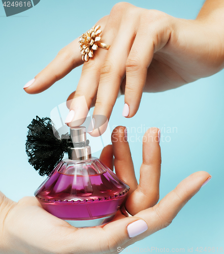 Image of woman hands holding bottle of perfume pink manicure and jewelry on blue background, luxury concept