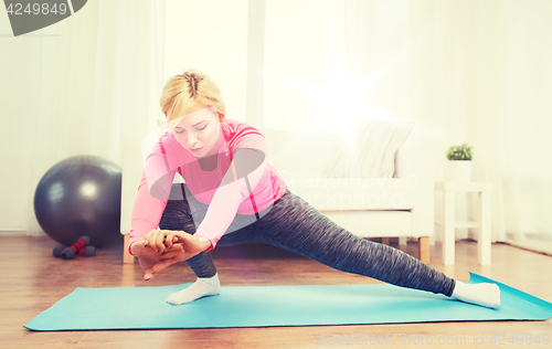 Image of woman stretching leg on mat at home
