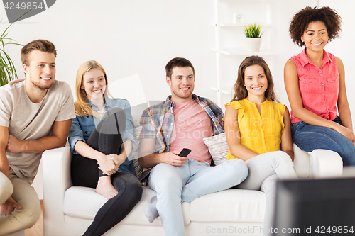 Image of happy friends with remote watching tv at home