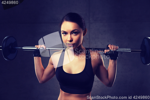 Image of young woman flexing muscles with barbell in gym