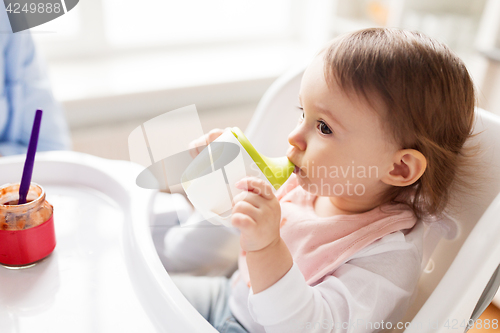 Image of baby drinking from spout cup in highchair at home