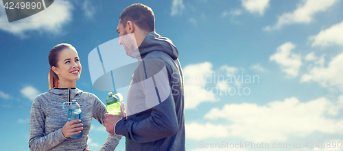 Image of smiling couple with bottles of water over blue sky