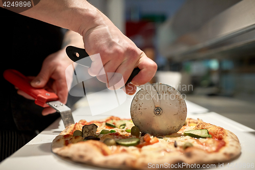 Image of cook cutting pizza to pieces at pizzeria