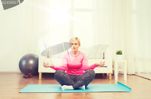 Image of happy woman stretching leg on mat at home