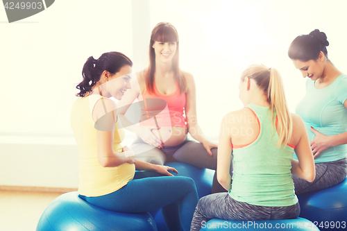 Image of happy pregnant women sitting on balls in gym