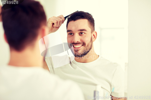 Image of happy man brushing hair  with comb at bathroom