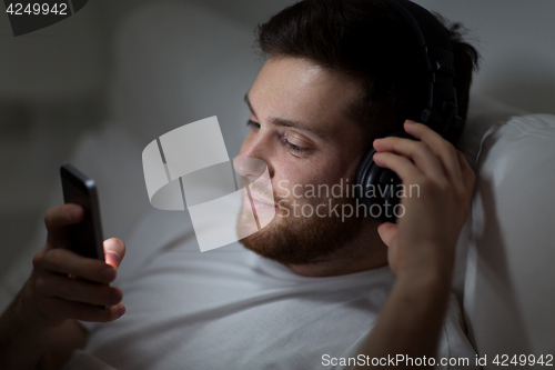 Image of man with smartphone and headphones in bed at night