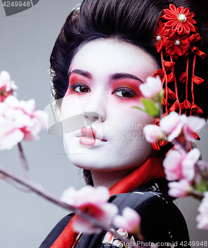 Image of young pretty geisha in black kimono among sakura, asian ethno close up