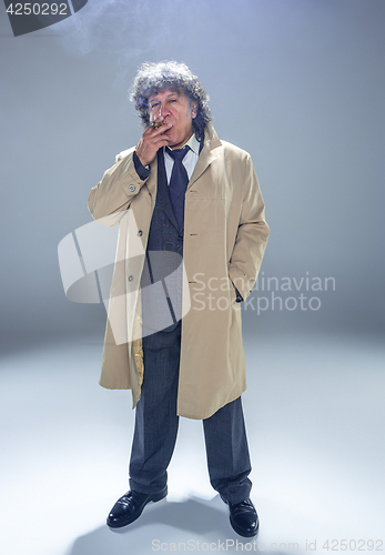 Image of The senior man with cigar as detective or boss of mafia on gray studio background