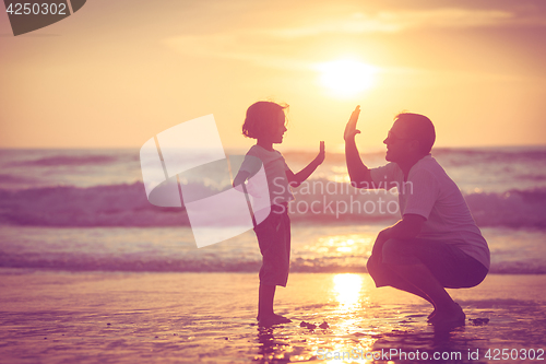 Image of Father and son playing on the beach at the sunset time.