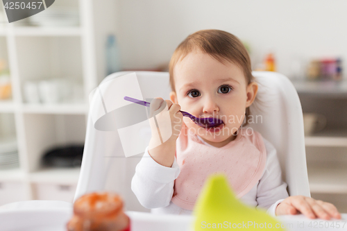 Image of baby girl with spoon eating puree from jar at home